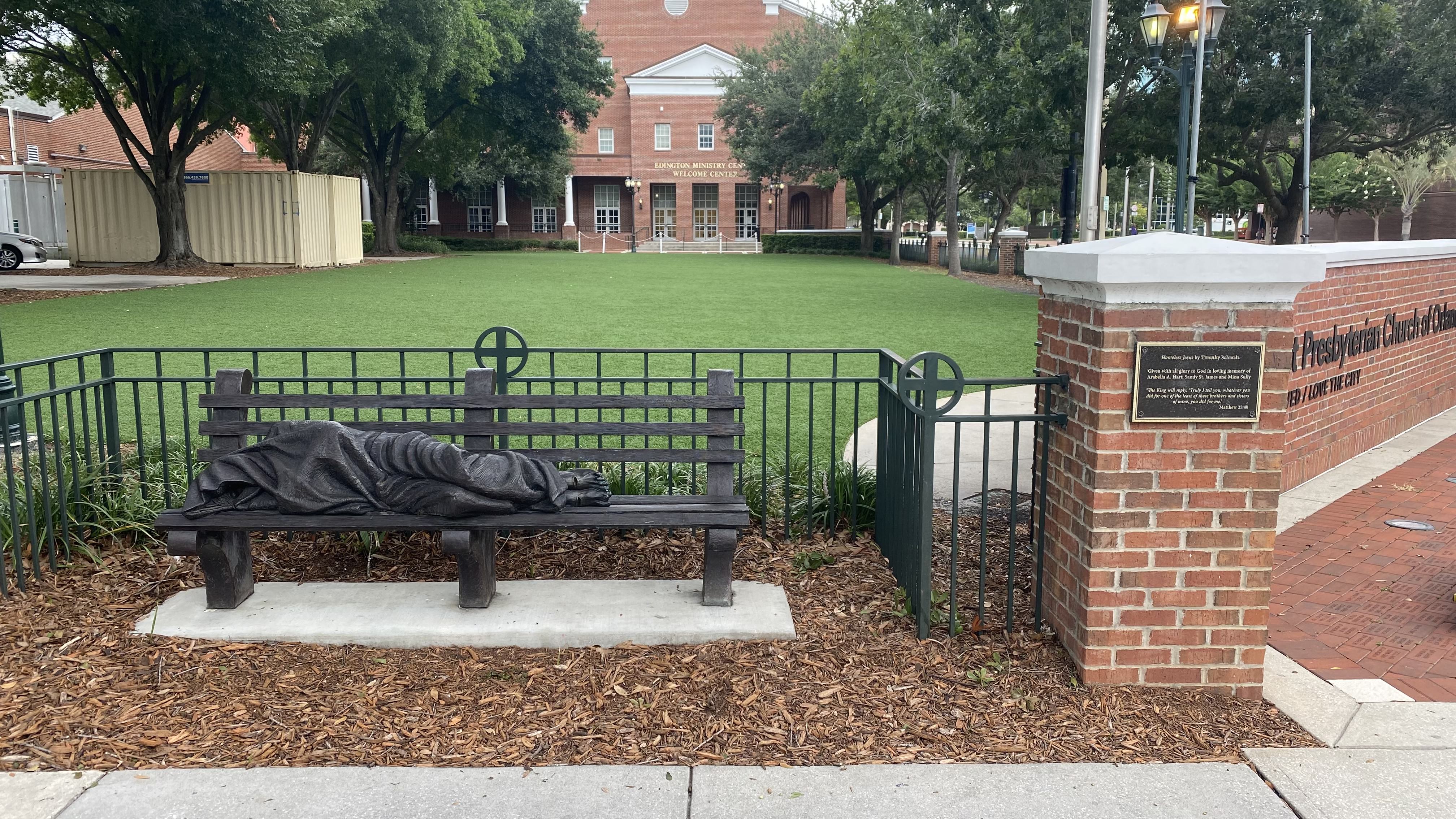 A photo depicting a man in rags huddled on a bench.